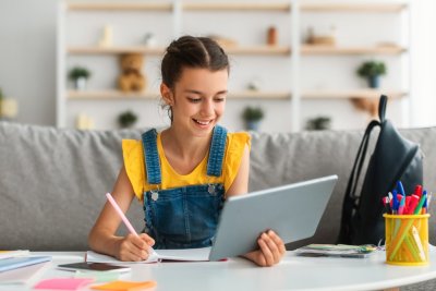Dívka drží v ruce tablet a v druhé ruce pero, sedí u stolu