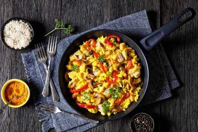 Paella v pánvi na stole, vedle misky s rýží, kurkumou a černým pepřem