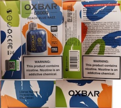 Bílé krabičky s modrými, zelenými a oranžovými skvrnami obsahující elektronické cigarety Oxbar