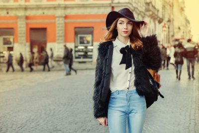 Dívka v úzkých džínách, stylové halence a klobouku stojí na chodníku