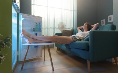Žena sedí na gauči a nohy má u otevřené lednice.