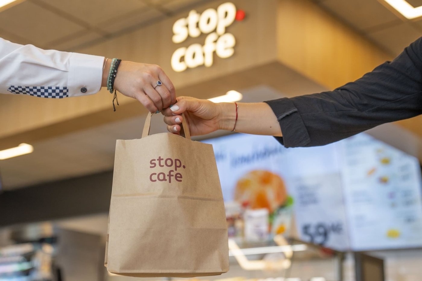 Pracovník kavárny Stop Cafe podává zákazníkovi objednávku v papírové tašce