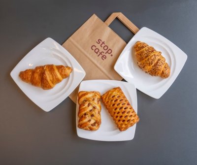 Sladké a slané pečivo na bílých talířích a papírová taška s logem Stop Cafe