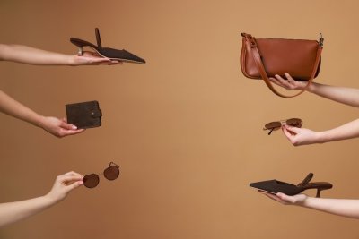 Šest dámských rukou držících hnědé módní doplňky na světle hnědém pozadí