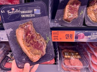 Ruka držící balený hovězí steak v supermarketu před regálem masných výrobků