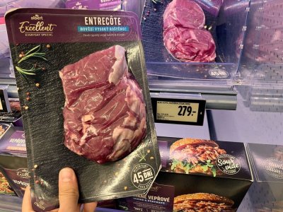 Ruka držící balený hovězí steak v supermarketu před regálem masných výrobků
