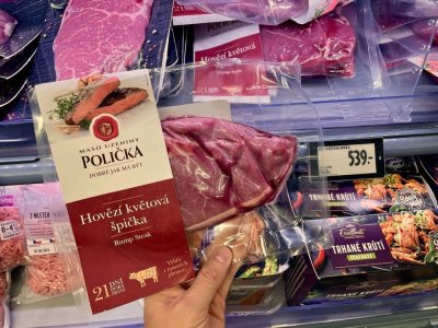 Ruka držící balený hovězí steak v supermarketu před regálem masných výrobků