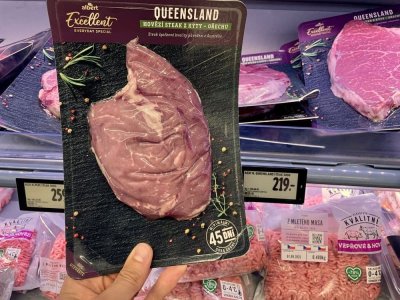Ruka držící balený hovězí steak v supermarketu před regálem masných výrobků