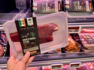 Ruka držící balený hovězí steak v supermarketu před regálem masných výrobků
