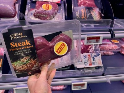 Ruka držící balený hovězí steak v supermarketu před regálem masných výrobků