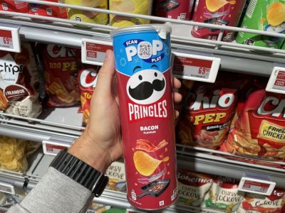 Ruka držící balení Pringles před regálem se slanými pochutinami v supermarketu