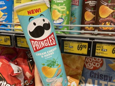 Ruka držící balení Pringles před regálem se slanými pochutinami v supermarketu