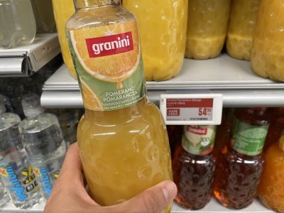 Ruka držící pomerančový džus před regálem v supermarketu