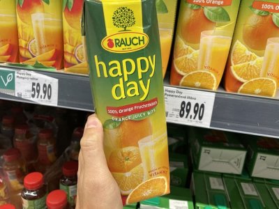 Ruka držící pomerančový džus před regálem v supermarketu