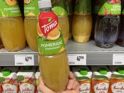 Ruka držící pomerančový džus před regálem v supermarketu