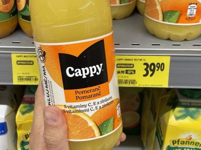 Ruka držící pomerančový džus před regálem v supermarketu