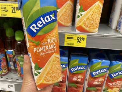 Ruka držící pomerančový džus před regálem v supermarketu