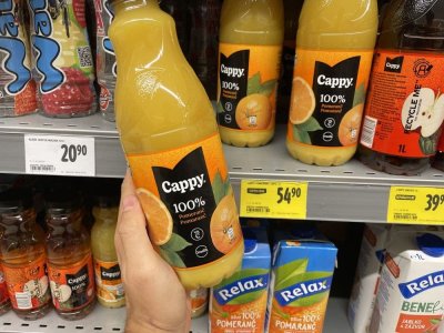 Ruka držící pomerančový džus před regálem v supermarketu