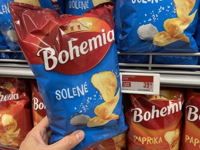 Ruka držící solené brambůrky před regálem v supermarketu