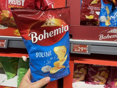Ruka držící solené brambůrky před regálem v supermarketu