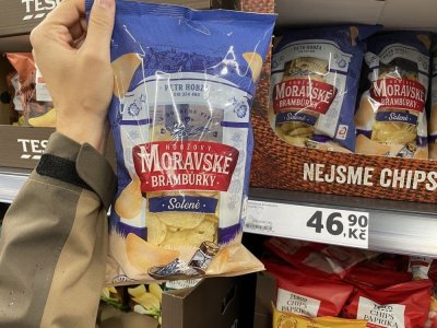 Ruka držící solené brambůrky před regálem v supermarketu