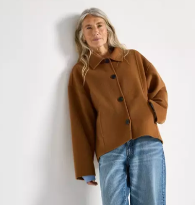 Starší modelka v džínách a hnědém krátkém kabátu