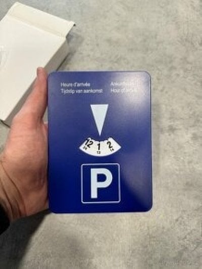Mužská ruka drží modré parkovací hodiny s bílým ciferníkem.