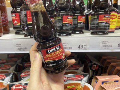 Ruka držící sójovou omáčku před regálem v supermarketu