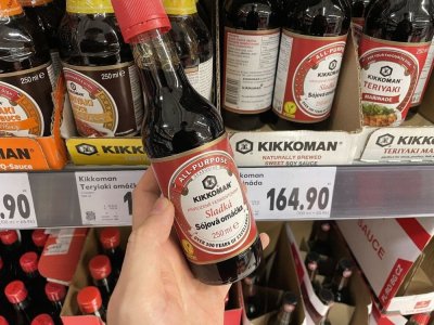 Ruka držící sójovou omáčku před regálem v supermarketu
