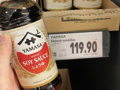 Ruka držící sójovou omáčku před regálem v supermarketu