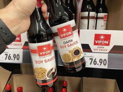Ruka držící sójovou omáčku před regálem v supermarketu