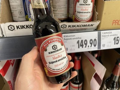 Ruka držící sójovou omáčku před regálem v supermarketu
