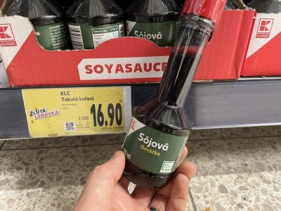 Ruka držící sójovou omáčku před regálem v supermarketu