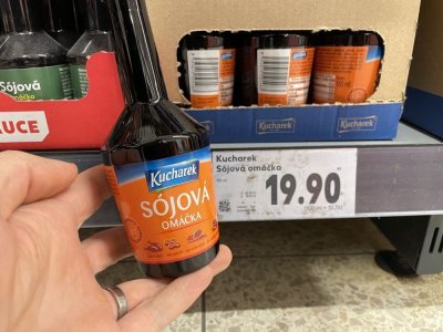 Ruka držící sójovou omáčku před regálem v supermarketu