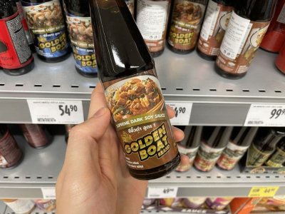 Ruka držící sójovou omáčku před regálem v supermarketu