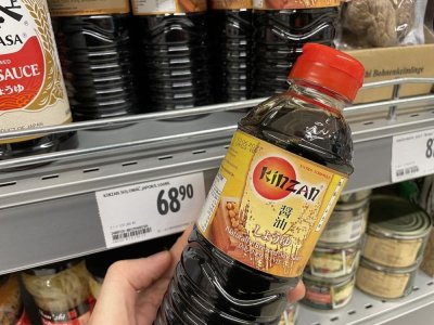 Ruka držící sójovou omáčku před regálem v supermarketu