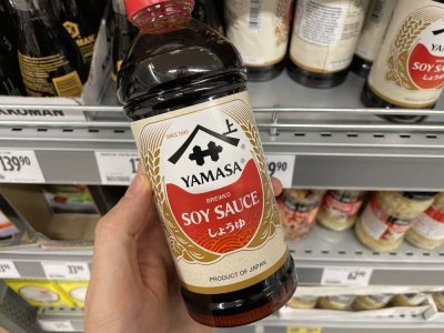Ruka držící sójovou omáčku před regálem v supermarketu