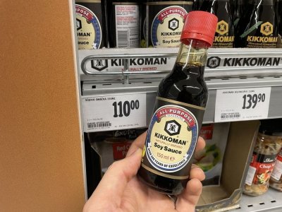 Ruka držící sójovou omáčku před regálem v supermarketu