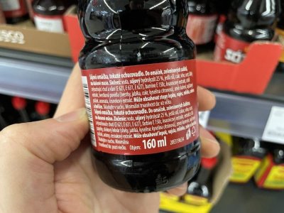 Ruka držící sójovou omáčku před regálem v supermarketu