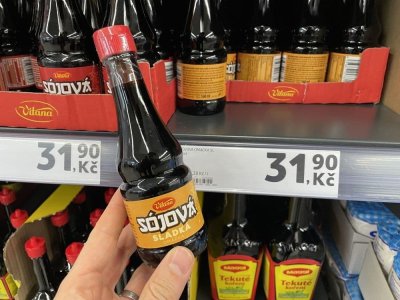 Ruka držící sójovou omáčku před regálem v supermarketu