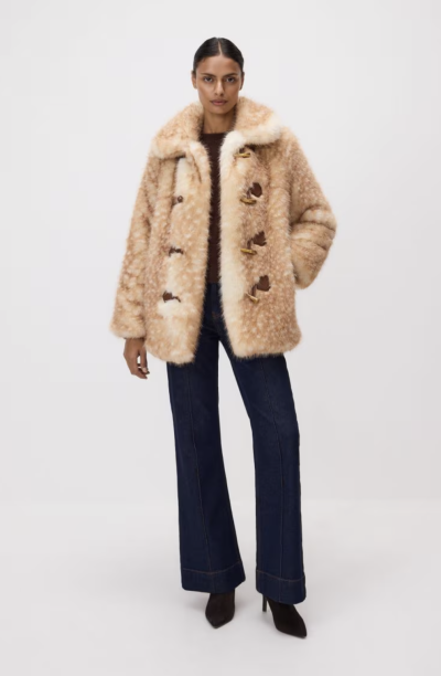 Modelka v béžové bundě z umělé kožešiny a černých úzkých kalhotách