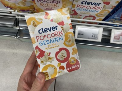 Ruka držící balení popcornu před regálem supermarketu