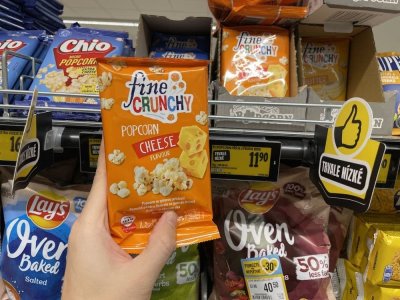 Ruka držící balení popcornu před regálem supermarketu