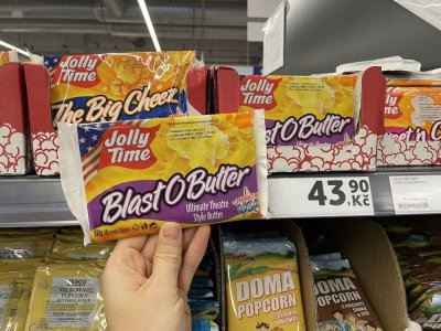 Ruka držící balení popcornu před regálem supermarketu