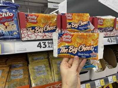 Ruka držící balení popcornu před regálem supermarketu