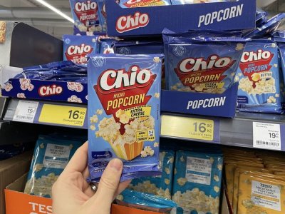 Ruka držící balení popcornu před regálem supermarketu