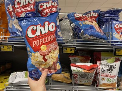 Ruka držící balení popcornu před regálem supermarketu