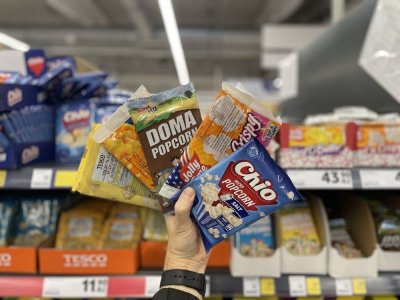 Ruka držící pět různých balení popcornu před regálem supermarketu