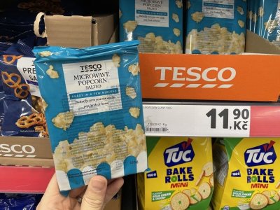 Ruka držící balení popcornu před regálem supermarketu