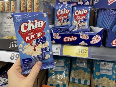 Ruka držící balení popcornu před regálem supermarketu